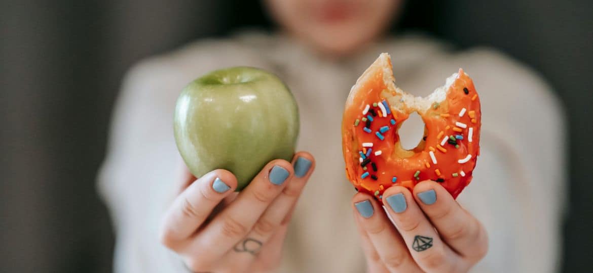 Woman showing apple and bitten doughnut